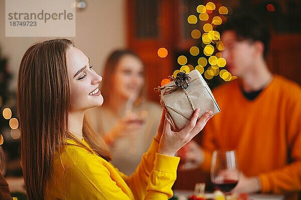 Junge Person  die einem Freund ein eingepacktes Geschenk gibt  während sie am Tisch sitzt und gemeinsam Weihnachten feiert