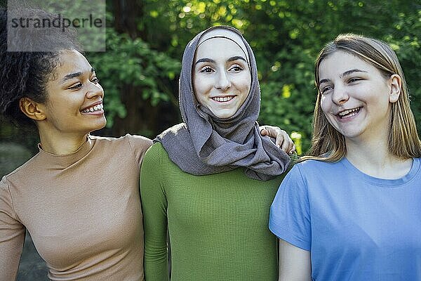 Multiracial junge Teenager weibliche Freunde zu Fuß in den Park lachen und Spaß haben zusammen. Diversität und Freundschaft Konzept