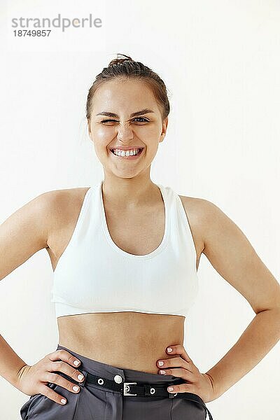 Junge Brünette weiblich mit Hand auf Taille Ziehen und Dehnen stilvolle crop top gegen weißen Hintergrund