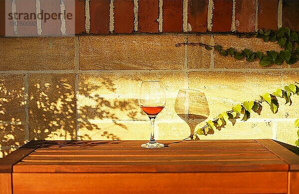 Glas Weißwein auf rustikalen Holztisch und Blumentöpfe auf der Terrasse außerhalb mit Weinberg Hügel Landschaft am sonnigen Tag Morgen im Sommer Zeit