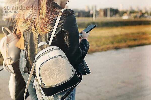 Glückliche junge Frauen mit Mobiltelefonen  die auf dem Bürgersteig spazieren gehen und an einem sonnigen Wochenendtag auf einer Straße in der Stadt lächeln