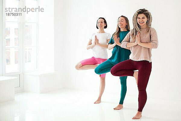 Glückliche junge Frauen meditieren lächelnd gegen eine weiße Wand während einer Yoga Sitzung