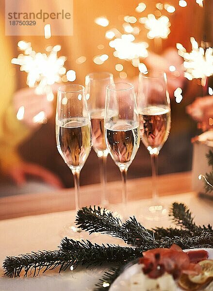 Gläser Champagner auf dem Tisch mit verschwommenen Hintergrund von festlichen Lichtern und eleganten Menschen Hände halten Weihnachten funkelt  Panoramablick von Freunden feiern Silvester oder Geburtstag mit Glück