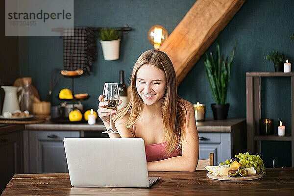 Glückliche junge Frau  die Weißwein trinkt  während sie mit ihrem Freund im Wohnzimmer sitzt und per Video chattet