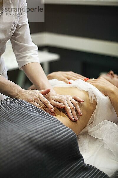 Teilansicht eines Masseurs bei der Bauchmassage einer Frau auf dem Massagetisch
