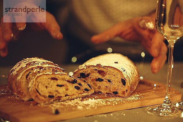 Männliche Hände nehmen geschnittenen traditionellen Weihnachtsstollen mit Puderzucker  selektiver Fokus. Weihnachten Brot gebacken mit getrockneten Früchten auf Schneidebrett in der Nähe Glas Champagner. Nahaufnahme von Weihnachtsstollen