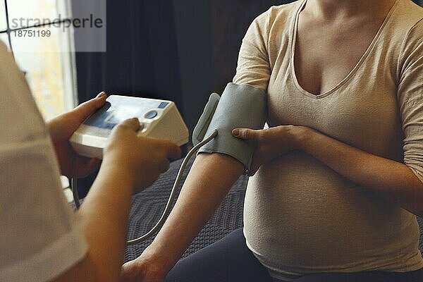 Ein Arzt mißt den Blutdruck einer schwangeren Frau bei einem Hausbesuch  ein Therapeut untersucht die werdende Mutter bei einem Termin zur Schwangerschaftsvorsorge im Krankenhaus  Ausschnitt. Bluthochdruck in der Schwangerschaft