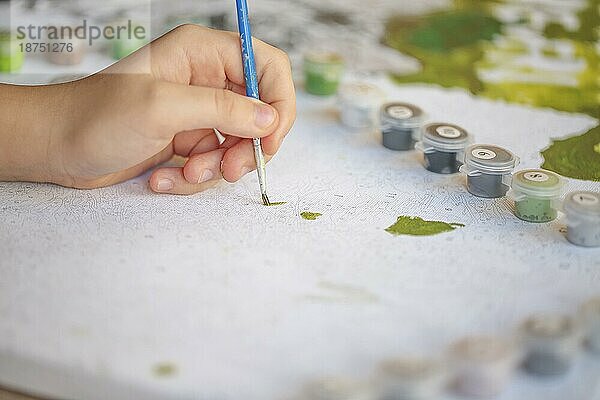 Unscharfes  beschnittenes Foto einer weiblichen Hand  die mit einem Pinsel auf Papier malt  selektiver Fokus auf Acrylfarben in Plastikdosen  die in einer Reihe entsprechend den Farbtönen im Vordergrund angeordnet sind. Konzept für Kunsttherapie und Hobby