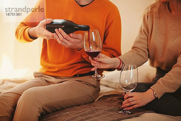 Junger Mann und Frau umarmen sich und genießen Rotwein bei einem romantischen Date zu Hause