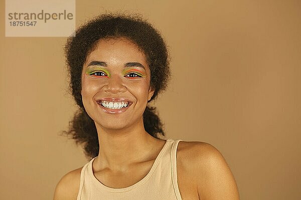 Schönheit Mode Porträt der attraktiven jungen afrikanischen amerikanischen Frau  schöne Glamour Modell mit stilvollen Neon Farbe Make up  Blick in die Kamera mit hellen Lächeln isoliert über beige Studio Hintergrund