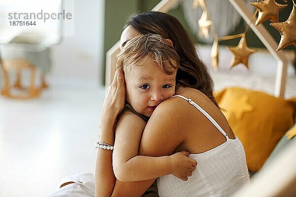 Junge Frau Mutter drückt Liebe zu kleinen Baby  sitzt auf dem Bett mit schlafenden Kind in den Händen und küsst es in die Stirn  zarte Foto der bedingungslosen Liebe zwischen Mutter und Sohn
