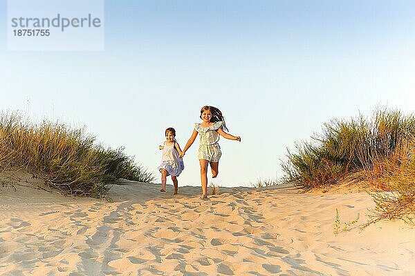 Zwei glückliche fröhliche kleine Schwestern laufen Hand in Hand auf Sand auf sonnigen Abend Strand  lustige Mädchen lachend und lächelnd verbringen Zeit mit der Familie am Meer. Reisen und Sommerurlaub Konzept
