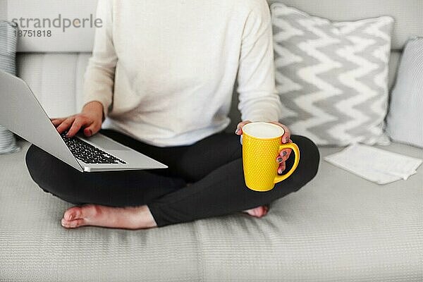 Glückliches junges Mädchen Freiberufler mit gelben Kaffeetasse arbeiten mit Laptop auf dem Sofa zu Hause