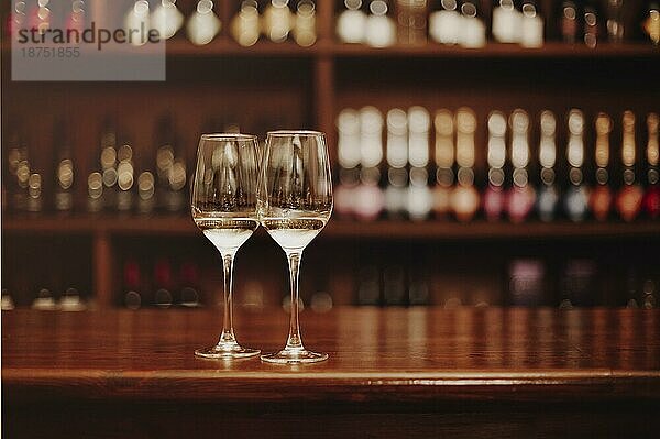 Zwei Gläser mit Weißwein auf dem hölzernen Stehtisch. Fotos in warmen Farben. Fokus auf das Glas Wein. Valentinstag  Datum  Liebe  Feier