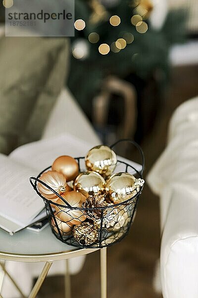 Vertikale Aufnahme von vielen Weihnachtsbaum Spielzeug Gold dekorative Kugeln in Metallkorb  stehend auf dem Tisch im Wohnzimmer zu Hause während der Winterferien  selektiven Fokus. Urlaub Dekor Konzept