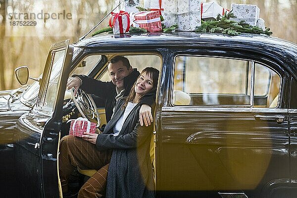 Verliebter Mann und Frau umarmen sich in einem Retroauto mit Weihnachtsgeschenken auf dem Dach im Park