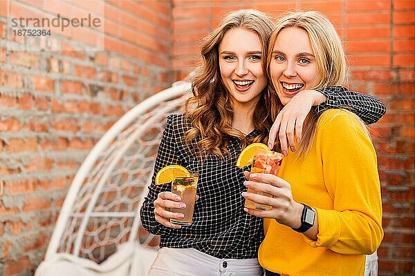Zwei junge Frauen trinken gesunde Getränke im Freien. Glückliche Freundinnen mit Zitrus Cocktails auf dem Dach Party