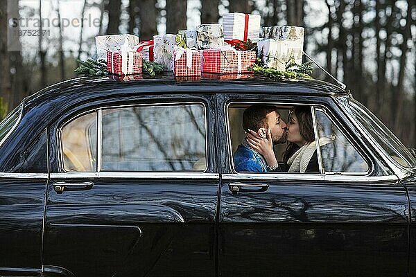 Verliebter Mann und Frau umarmen sich in einem Retroauto mit Weihnachtsgeschenken auf dem Dach im Park