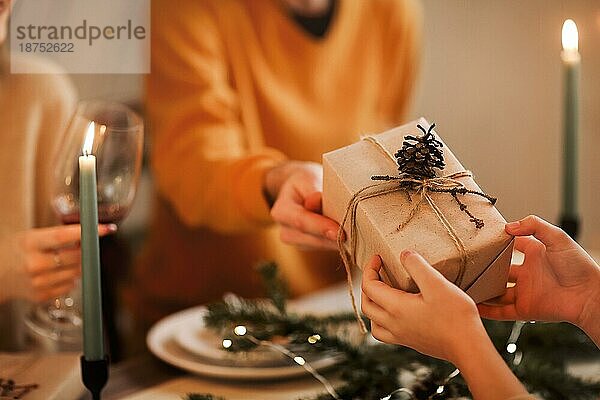 Weichzeichner einer nicht erkennbaren Person  die einem Freund ein eingepacktes Geschenk gibt  während sie am Tisch sitzt und gemeinsam Weihnachten feiert
