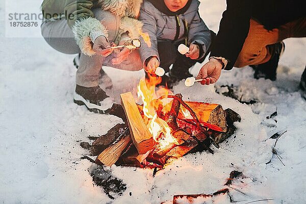 Unbekannte Eltern und Kind braten Marshmallows am Lagerfeuer  während sie im Winterwochenende Zeit in der Natur verbringen