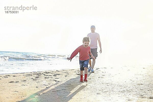 Liebevoller Vater spielt mit seiner entzückenden kleinen Tochter am Strand  Vater und Kind verbringen Zeit im Freien zusammen  sonniges Meer im Hintergrund. Parenting Konzept
