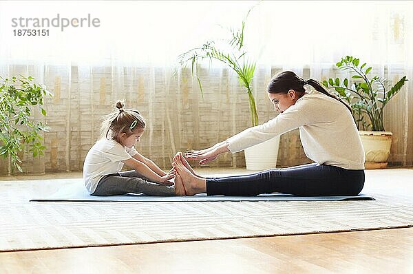Mutter und kleine Tochter sitzen auf einer Matte und machen Übungen beim Aufwärmen und gemeinsamen Training zu Hause