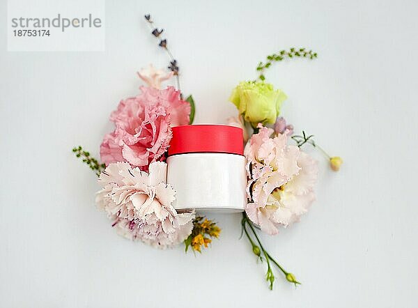 Draufsicht auf einen Tiegel mit Gesichtscreme aus natürlichen pflanzlichen Inhaltsstoffen  Ölen und Kräutern  Nelken und Rosenblüten auf weißem leeren Hintergrund  vertikale Aufnahme. Bio Kosmetik Konzept