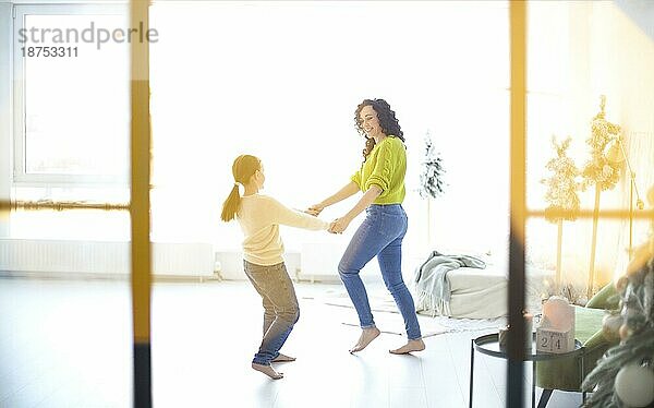 Glückliche Familie Mutter und kleines Mädchen Tochter hält die Hände und tanzen in hellen sonnigen Raum  Kind  das Spaß mit lächelnden positiven Mutter  während die Freizeit zusammen am Wochenende zu Hause