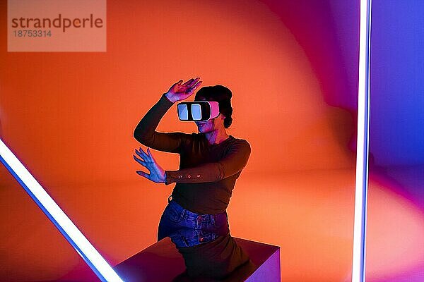 Glückliche Frau mit VRheadset lächelt und erkundet die virtuelle Realität unter roter Neonbeleuchtung in einem futuristischen Raum