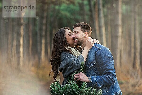 Glücklicher Mann und Frau in warmer Kleidung  die zusammen einen Tannenbaum tragen und auf einem Waldweg gehen