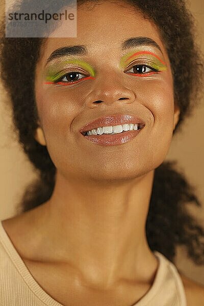 Schönheit Mode Porträt der attraktiven jungen afrikanischen amerikanischen Frau  schöne Glamour Modell mit stilvollen Neon Farbe Make up  Blick in die Kamera mit hellen Lächeln isoliert über beige Studio Hintergrund