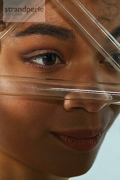 Afrikanische weibliche Schönheit. Closeup Porträt der jungen schönen schwarzen lockige Frau mit sauberen gesunden Haut Blick durch Dreieck aus Glas Reagenzgläser  vertikale Aufnahme. Hautpflege Konzept