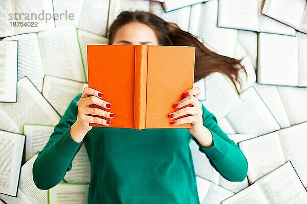 Draufsicht auf eine anonyme Studentin  die während der Prüfungsvorbereitung auf Büchern liegt und liest