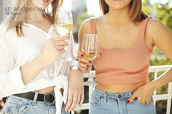Zwei stilvolle glückliche Frauen versammeln sich im Sommer zu einer Party und genießen die gemeinsame Zeit beim Trinken von Weißwein Nahaufnahme