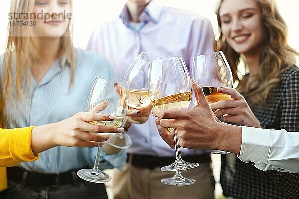Eine Gruppe anonymer Personen stößt während einer Party auf dem Dach mit Weingläsern an und bringt einen Toast aus