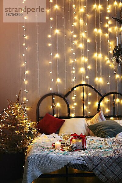 Tablett mit Dekorationen und Geschenkbox auf bequemen Bett in gemütlichen Schlafzimmer für Weihnachtsfeier in der Nacht dekoriert platziert