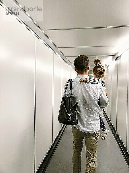 Rückenansicht eines Mannes mit einer kleinen Tochter  die entlang einer Metallbrücke für das Einsteigen in ein Flugzeug läuft