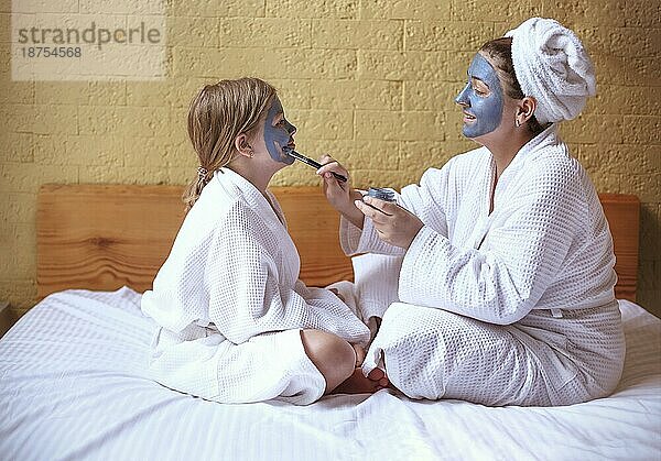 Glückliche Familie Mutter und Baby Tochter machen Gesichtsmaske  Hautpflege zusammen