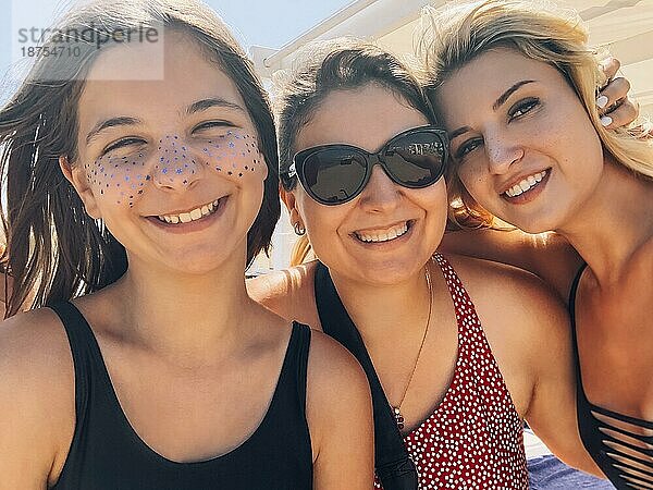 Gesellschaft freundlicher Frauen in Badekleidung  die sich am Strand an einem sonnigen Tag entspannen und ein Selfie machen  während sie lächeln und in die Kamera schauen