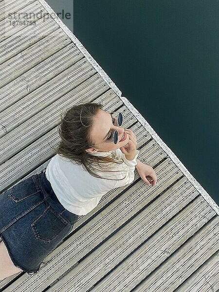 Junge brünette Frau liegt auf dem Kai und spritzt sauberes Wasser des Sees am Sommertag