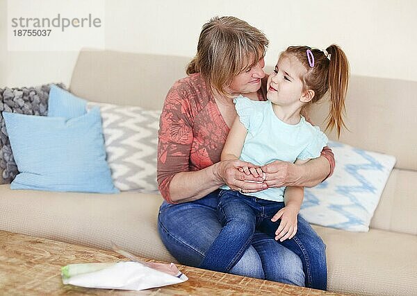 Eine Frau desinfiziert die Hände ihrer kleinen Enkelin mit einem antibakteriellen Feuchttuch  während sie zu Hause auf dem Sofa sitzt