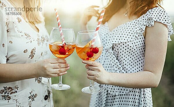 Anonyme Frau  die einen Becher mit einem alkoholischen Cocktail mit Kirschen und einem gestreiften Strohhalm vor einem unscharfen Landschaftshintergrund trägt