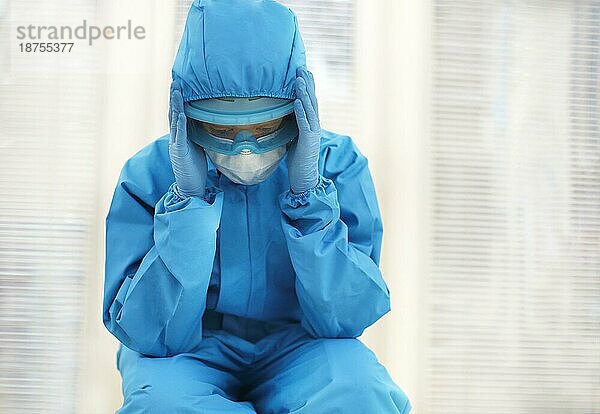 Müde Ärztin in persönlicher Schutzausrüstung (PSA)  deprimiert nach schwieriger  stressiger Schicht während der Covid 19 Pandemie  sitzt auf dem Boden im Krankenhaus. Überfordertes Gesundheitspersonal