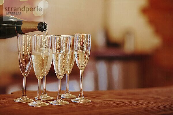 Unbekannter Männchen füllt Weinglas mit Sekt  während er auf einem Banketttisch mit brennenden Kerzen während einer Weihnachtsfeier zu Hause steht