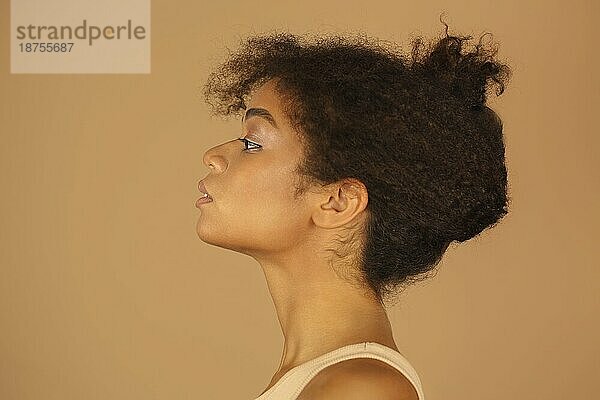 Schönheitsprofilporträt einer jungen selbstbewussten afroamerikanischen Frau mit gesunder klarer Haut und lockigem Haar vor braunem Studiohintergrund  Seitenansicht eines dunkelhäutigen weiblichen Modells mit natürlichem Make up