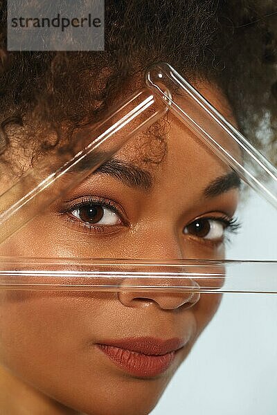 Afrikanische weibliche Schönheit. Closeup Porträt der jungen schönen schwarzen lockige Frau mit sauberen gesunden Haut Blick durch Dreieck aus Glas Reagenzgläser  vertikale Aufnahme. Hautpflege Konzept