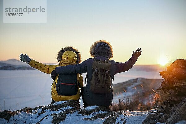 Romantisches Touristenpaar in warmer Wintersportkleidung mit Touristenrucksäcken in den verschneiten Bergen bei einem unglaublichen Sonnenuntergang. Ogoi Insel  Baikalsee. Familie  Ruhe