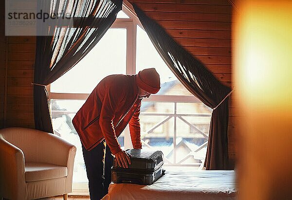 Stylish Hipster Reisenden Mann in roten Hut in Holzhaus Packen Koffer  Winter Reise Konzept  Platz für Text  gemütlichen Moment. Urlaub und Reisekonzept