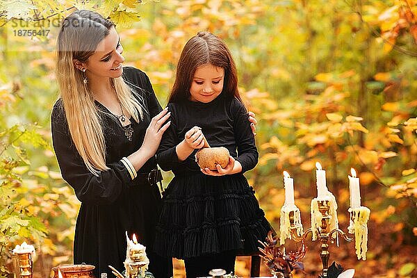 Glückliche Frau und Mädchen zerkleinern Kräuter im Mörser  während sie einen Zaubertrank während der Halloween Feier am Herbsttag im Wald zubereiten