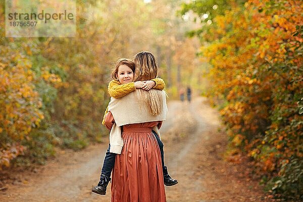 Junge Familie  Mutter und kleiner Sohn  bei einem Spaziergang im Herbstwald  Mutter und Kind halten sich an den Händen und gehen einen Weg entlang  der mit gelben Blättern bedeckt ist  und verbringen Zeit in der schönen Natur